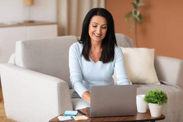 Reife Frau sitzt auf Couch und arbeitet am Computer — Stockfoto