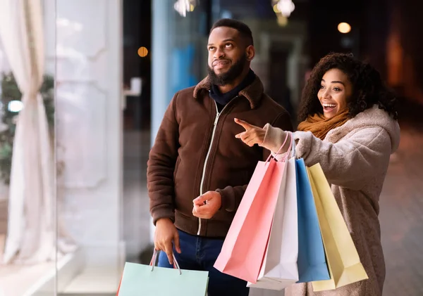 Excited black woman with bags pointing at shop window — Stock Photo, Image