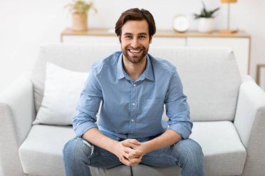 Koltukta oturan mutlu adam evdeki kameraya gülümsüyor.