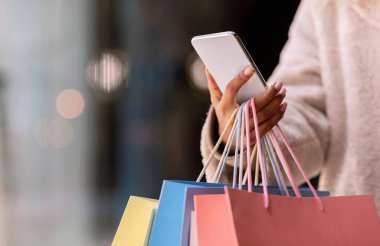 Akıllı telefon kullanan, alışveriş torbaları tutan mutlu siyah kadın.