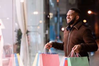 Alışveriş torbalarıyla alışveriş merkezine bakan siyah bir adam.