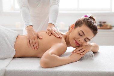 Tanımlanamayan masaj terapisti genç bayanın sırtını ovuyor.