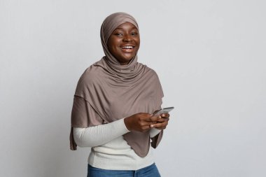 Mobil İletişim. Tesettürlü neşeli siyah kadın ellerinde akıllı telefonla poz veriyor.