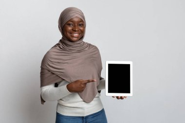 Siyah ekranlı dijital tableti işaret eden tesettürlü gülümseyen Afrikalı kadın