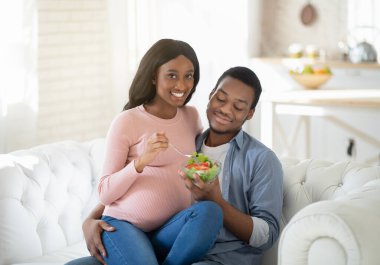 Hamilelik boyunca sağlıklı beslenme. Mutlu siyah erkek arkadaş ve hamile kız arkadaşı evde lezzetli sebze salatası yiyorlar.