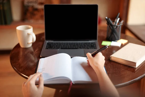 Mujer sentada en el escritorio usando el ordenador portátil, escribiendo en el cuaderno, pov — Foto de Stock