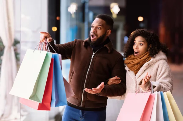 Excited black couple with shopping bags pointing at mall window — Stock Photo, Image