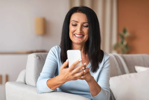 집에서 스마트폰을 사용하여 웃고 있는 장성 한 여자 — 스톡 사진