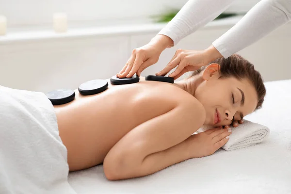 Giovane signora riceve massaggio con pietre calde al moderno centro benessere — Foto Stock