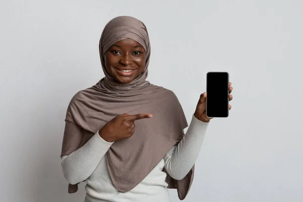 Oferta mobilna. Uśmiechnięta kobieta w hidżabie wskazując na smartfon z czarnym ekranem — Zdjęcie stockowe