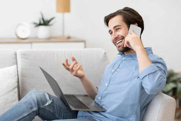 Cheerful Guy Talking On Phone Sitting With Laptop At Home — Stock Photo, Image