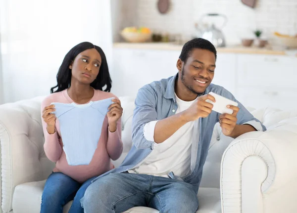 Concepto de adicción al gadget. Hombre negro egoísta jugando juegos en el teléfono celular, descuidando a su esposa expectante en casa — Foto de Stock