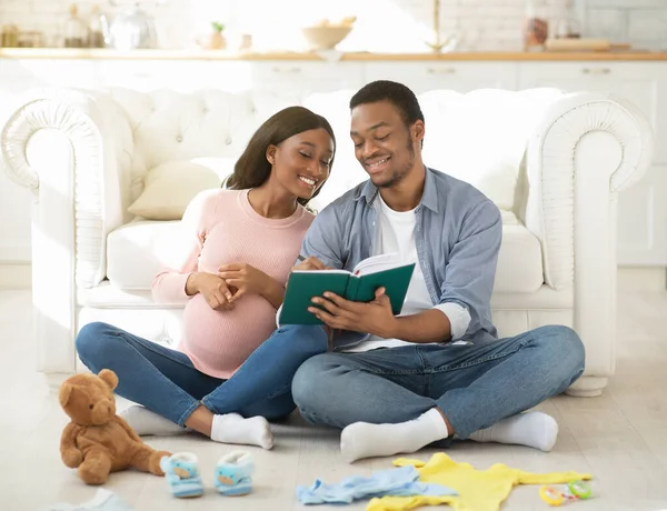 Alegre pareja negra haciendo una lista de cosas para bebés para el hospital de maternidad, escribiendo en un cuaderno en casa — Foto de Stock