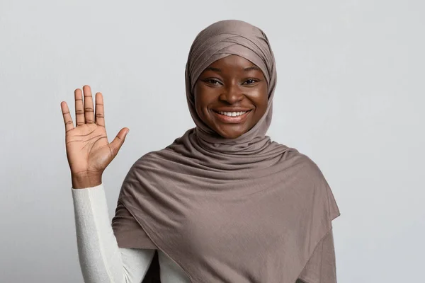Witaj, Gesture. Przyjazny czarny muzułmanin pani w chustce macha ręką przed kamerą — Zdjęcie stockowe