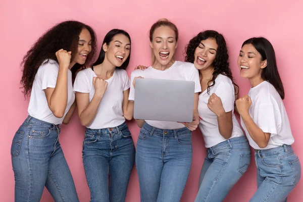Cinque donne che tengono in mano il computer portatile scuotendo pugni nella gioia, sfondo rosa — Foto Stock