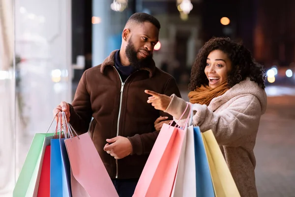 Excited black woman with shopping bags pointing at mall window — Stock Photo, Image