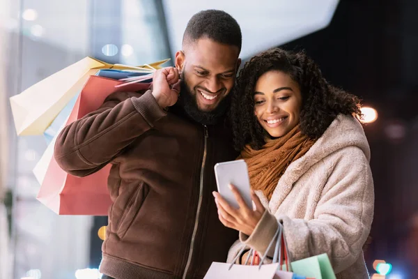 Retrato de feliz pareja afro usando smartphone con bolsas de compras —  Fotos de Stock