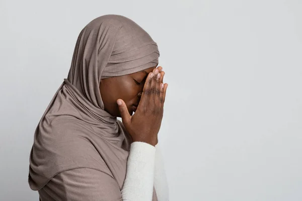 Perfil retrato de triste llorando mujer musulmana negra en hijab cubriendo la cara con las manos, de pie sobre fondo claro, panorama con espacio vacío — Foto de Stock