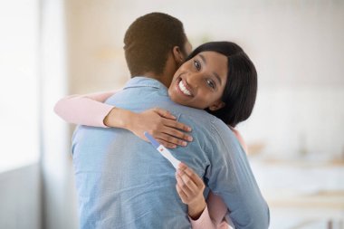 Pozitif hamilelik testi olan mutlu genç zenci kadın sevgili kocasına içeride sarılıyor.