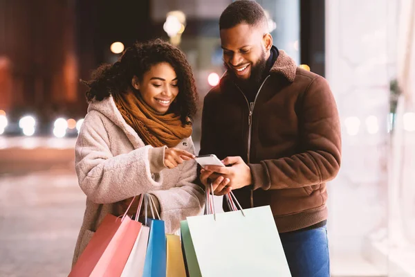 Portrait of happy black couple using smartphone holding shopping bags — Stock Photo, Image