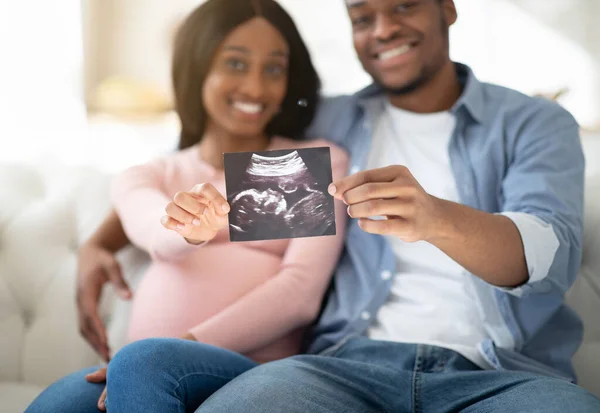 Jóvenes futuros padres sosteniendo la foto de su bebé nonato en casa, enfoque selectivo en las manos — Foto de Stock