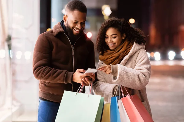 Portrait of happy black couple using phone holding shopping bags — Stock Photo, Image