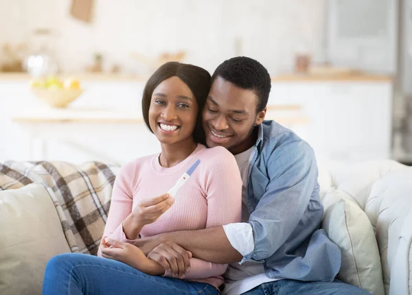 Keluarga muda Afrika Amerika belajar tentang masa depan anak mereka dari tes kehamilan di rumah, merangkul di sofa — Stok Foto