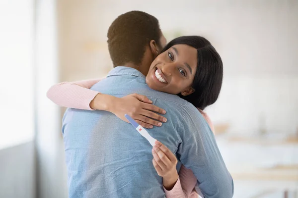 Feliz joven mujer negra con prueba de embarazo positiva abrazando a su amado marido en el interior — Foto de Stock