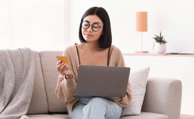 Gözlüklü Asyalı kadın dizüstü bilgisayar kartı kullanarak alışveriş yapıyor.