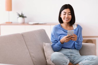 Gülümseyen Asyalı kadın evinde akıllı telefon kullanıyor.