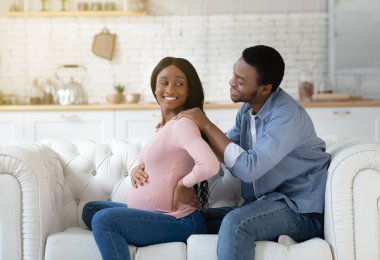 Hamilelik konsepti sırasında masaj. Evdeki rahat koltukta karısına masaj yapan düşünceli bir zenci.