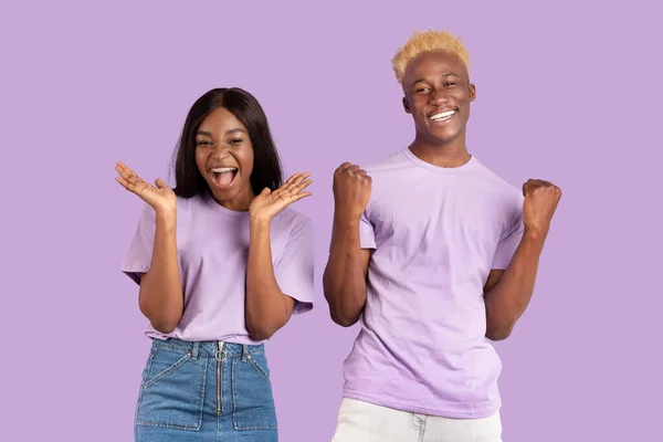 快乐的黑人夫妇一起庆祝成功，在紫丁香工作室的背景上做"是"的手势 — 图库照片
