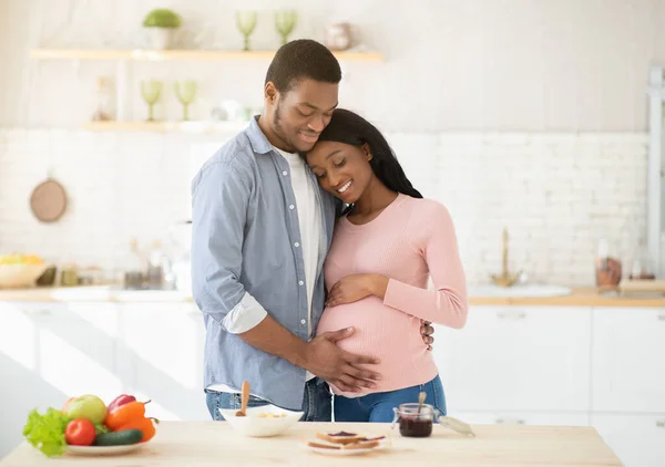 Tender homem negro tocando sua barriga mulheres grávidas ao fazer refeição na cozinha — Fotografia de Stock