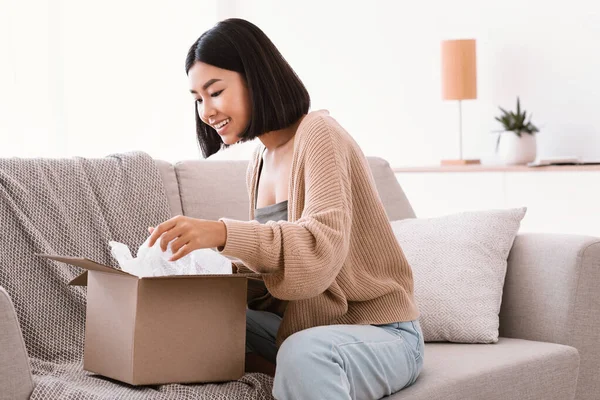 Glücklich asiatisch frau auspacken paket sitzen auf couch — Stockfoto