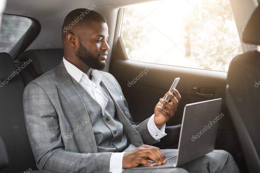 Handsome african businessman with laptop holding smartphone