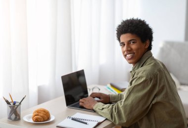 Genç mutlu adam evde uzaktan çalışmalar için dizüstü bilgisayar kullanıyor, ekranda tasarım için model alıyor.