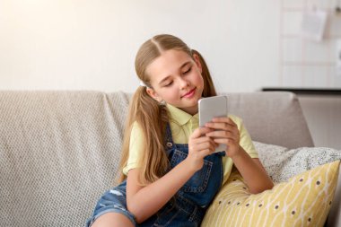 Akıllı telefonunu kanepede dinlenirken kullanan bir kız.