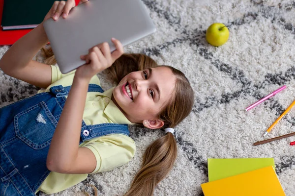 Menina deitada no tapete chão, segurando e usando tablet — Fotografia de Stock