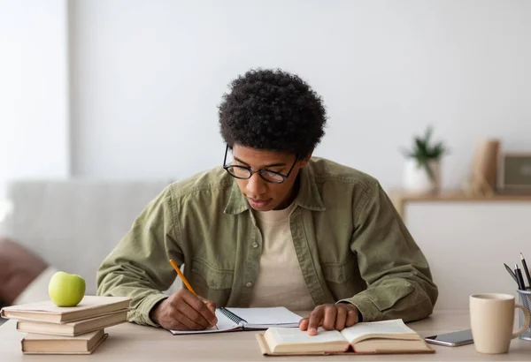 Aprendizaje remoto. Estudiante universitario negro tomando notas de un libro de texto, estudiando en casa durante el brote de coronavirus —  Fotos de Stock