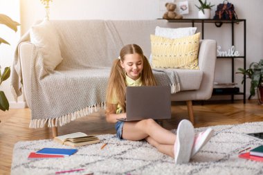 Kız yerde oturuyor ve bilgisayarını kullanıyor.