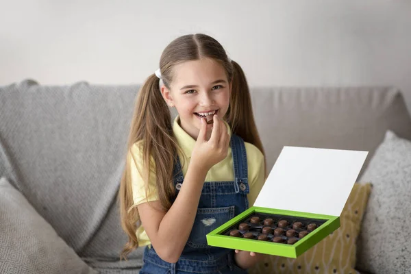 Chica comiendo caramelos de chocolate sentado en un sofá en casa — Foto de Stock
