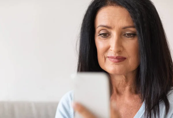 Улыбающаяся взрослая женщина с мобильного телефона у себя дома — стоковое фото