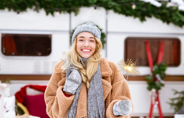 Alegre señora rubia posando con chispeante al aire libre cerca de autocaravana en el campamento de invierno —  Fotos de Stock