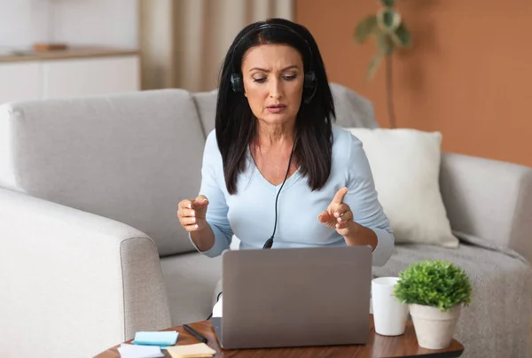 Serious woman sitting on sofa, having video call on computer — Stock Photo, Image