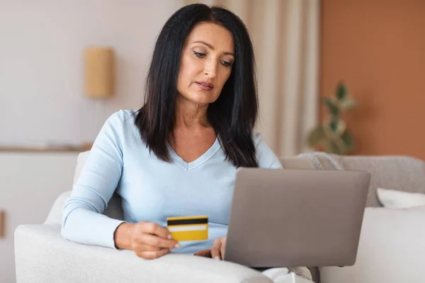 Зріла жінка робить покупки за допомогою ноутбука, що тримає кредитну картку — стокове фото