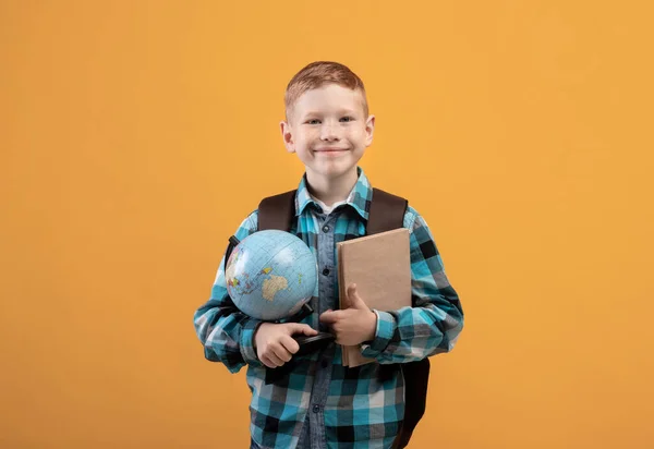 Estudante positivo com mochila segurando montão de livros e globo — Fotografia de Stock