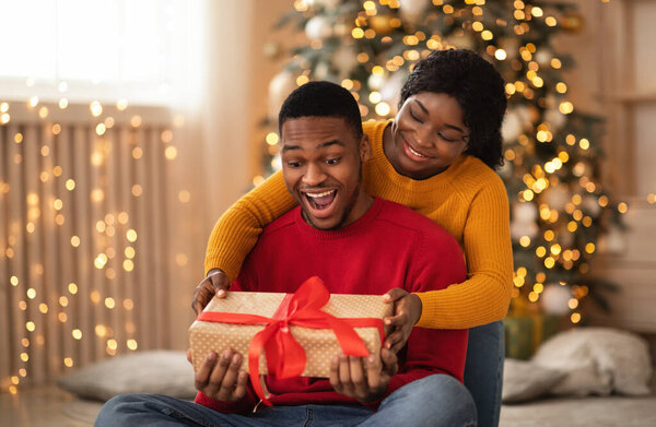 Surprised african american young husband hold box with gift and red ribbon