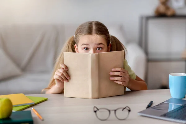 Chica asustada con los ojos abiertos escondidos detrás de un libro — Foto de Stock