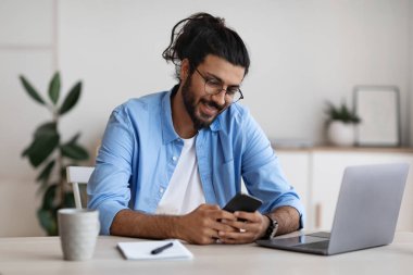 Batılı serbest çalışan adam evdeki masada oturuyor ve akıllı telefon kullanıyor.