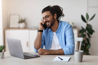 Batılı serbest çalışan adam cep telefonuyla konuşuyor ve evde dizüstü bilgisayarla çalışıyor.